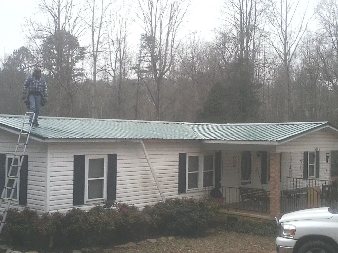 Worker on a ladder beside a new green metal roof on a ranch home in Ardsley On Hudson