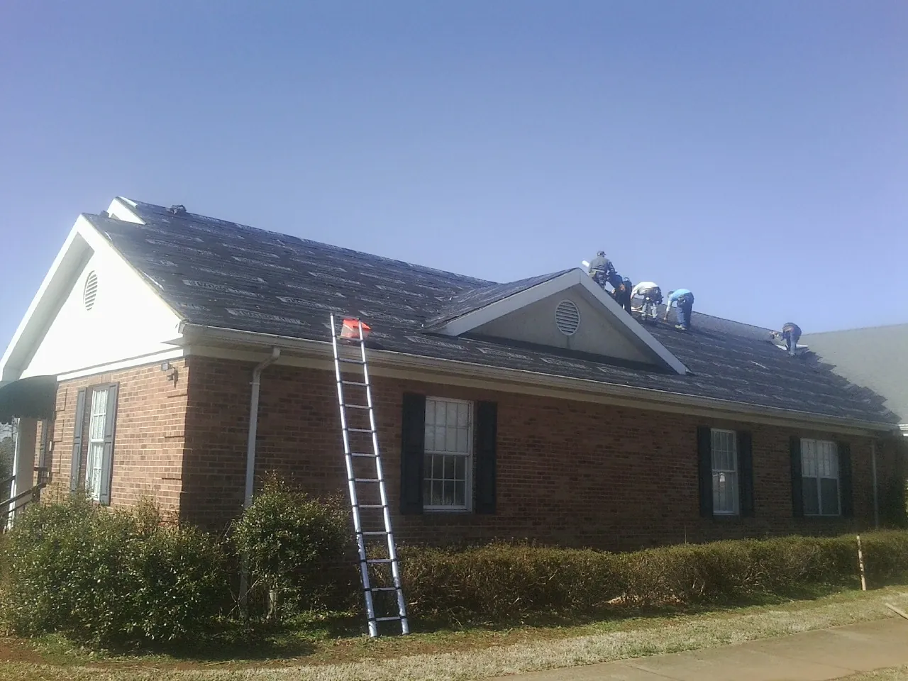 Crew tearing shingles off a brick ranch roof with a ladder set — Emergency Roof Repair work by our crew in Ardsley On Hudson
