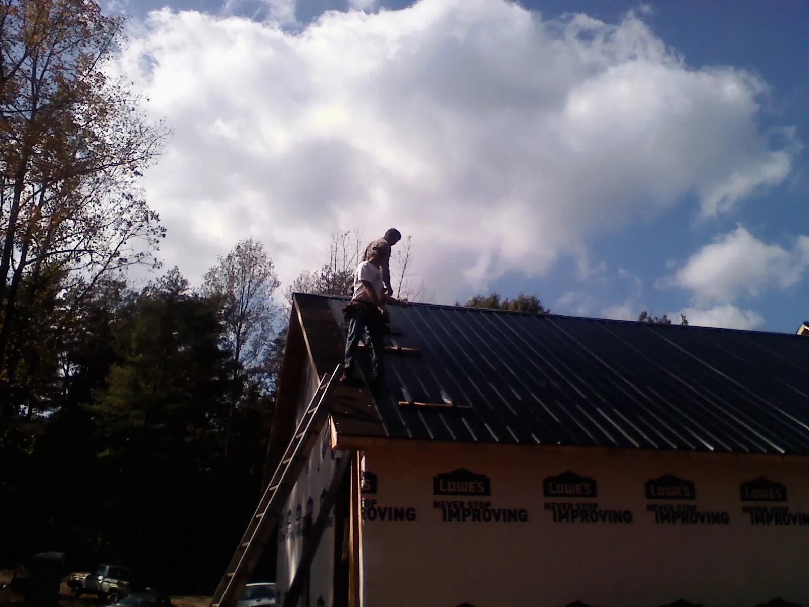 Roofer fastening dark metal panels high against a cloudy sky, from a Roof Inspection job in Ardsley On Hudson