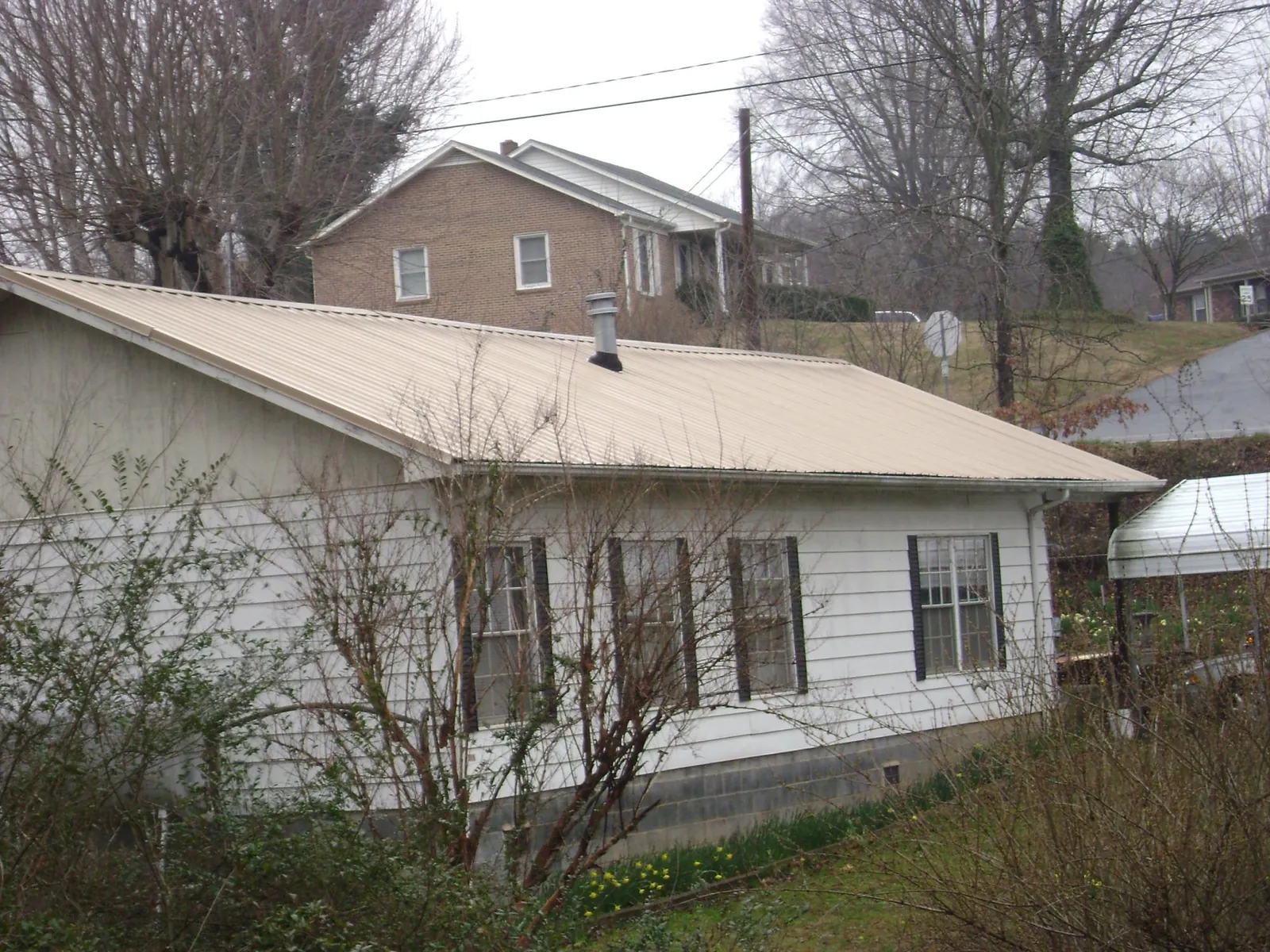 Tan metal roof on a white sided house set into a hillside — Commercial Roofing by Roofing Brothers in Ardsley On Hudson